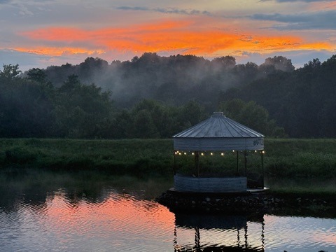 Grain-bin gazebo reflected in Tuckaway Lake beneath a vivid sunset